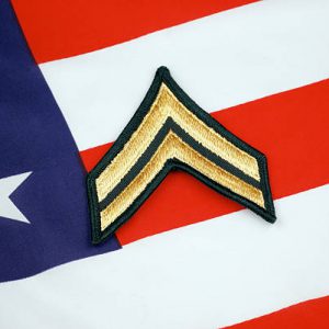 United States Army corporal rank insignia on American flag background.