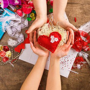Materials and tools for hand decoration for Valentine's Day on a sacking. Female hands give red heart in male hands.. Love and valentine concept.